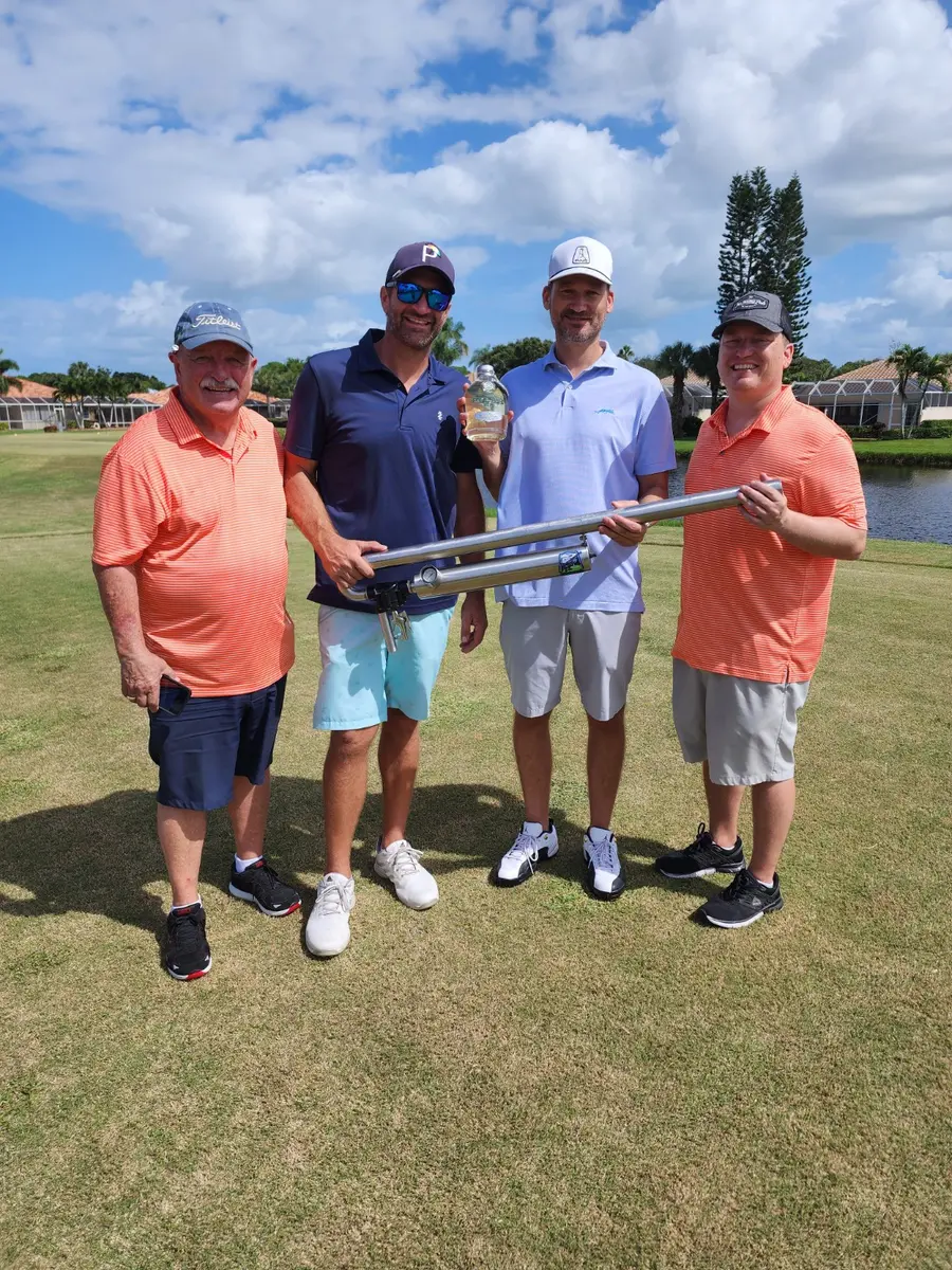 Golf foursome holding a ball launcher and prize bottle